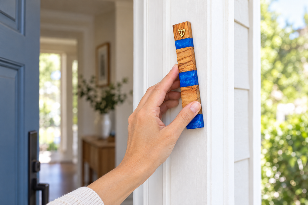 A hand placing an olive wood mezuzah case on the right side of a doorframe
