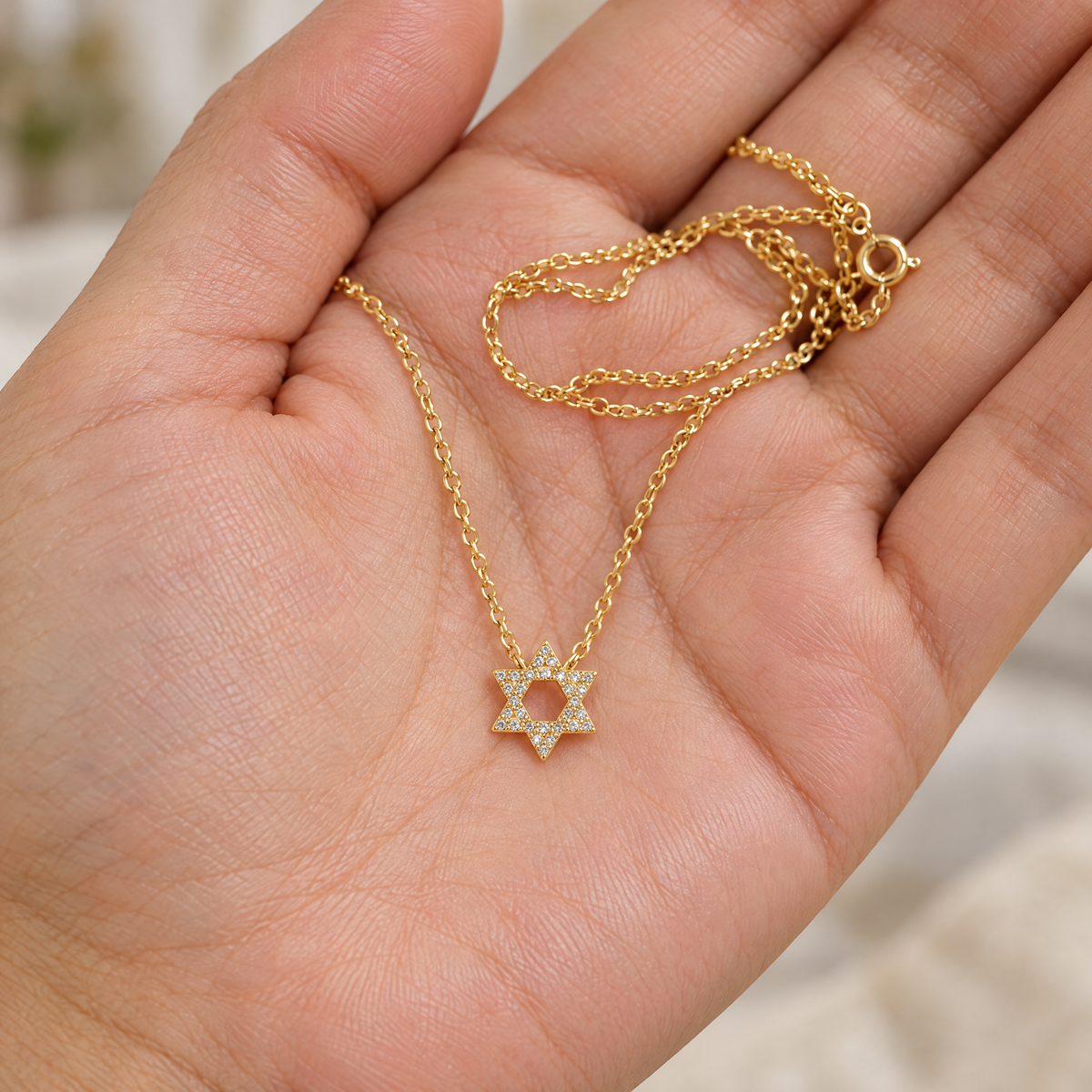 Gold Star of David necklace in the palm of a hand to show its size