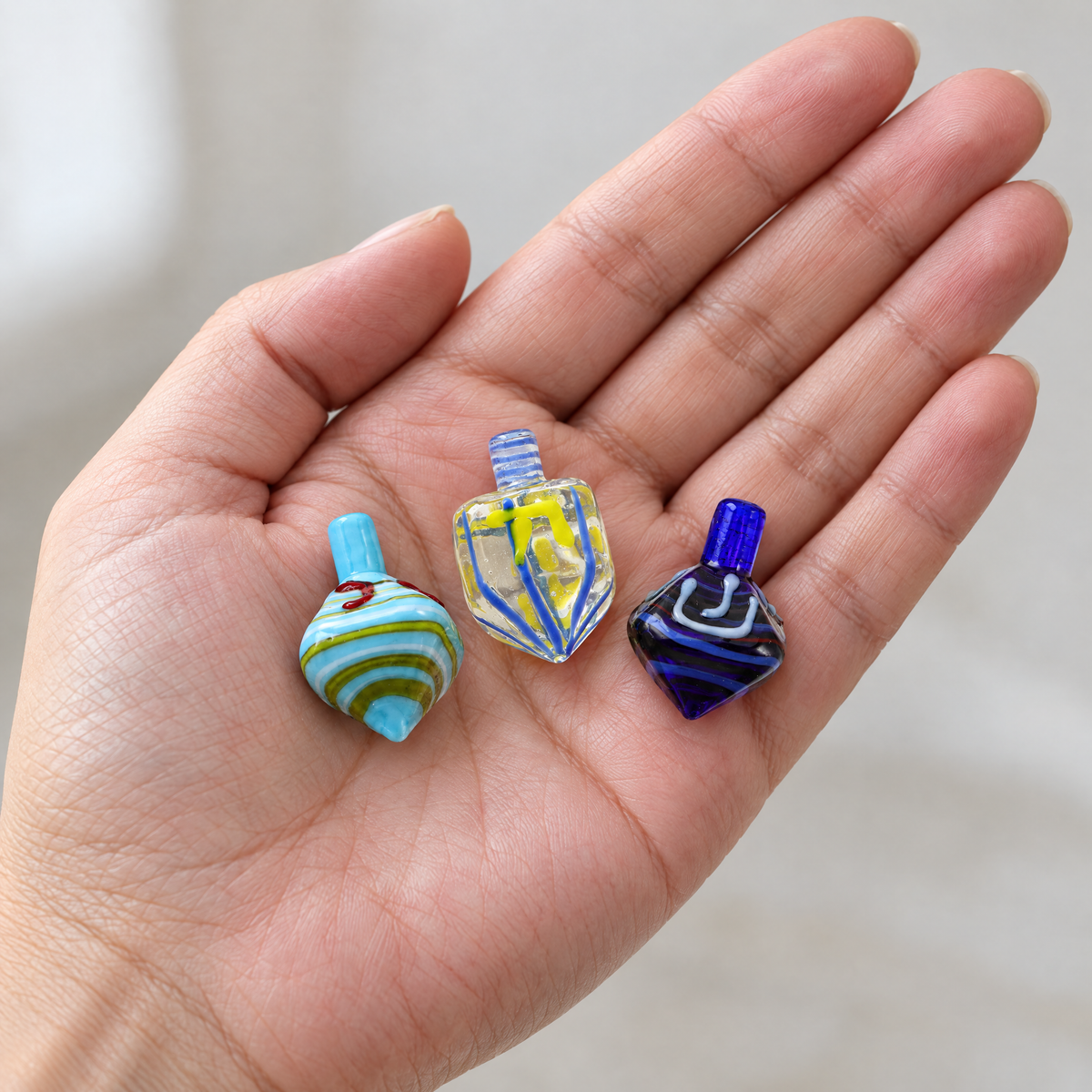 Glass dreidel set of 3 in the palm, shown at real size (3.5 to 4 cm tall each)