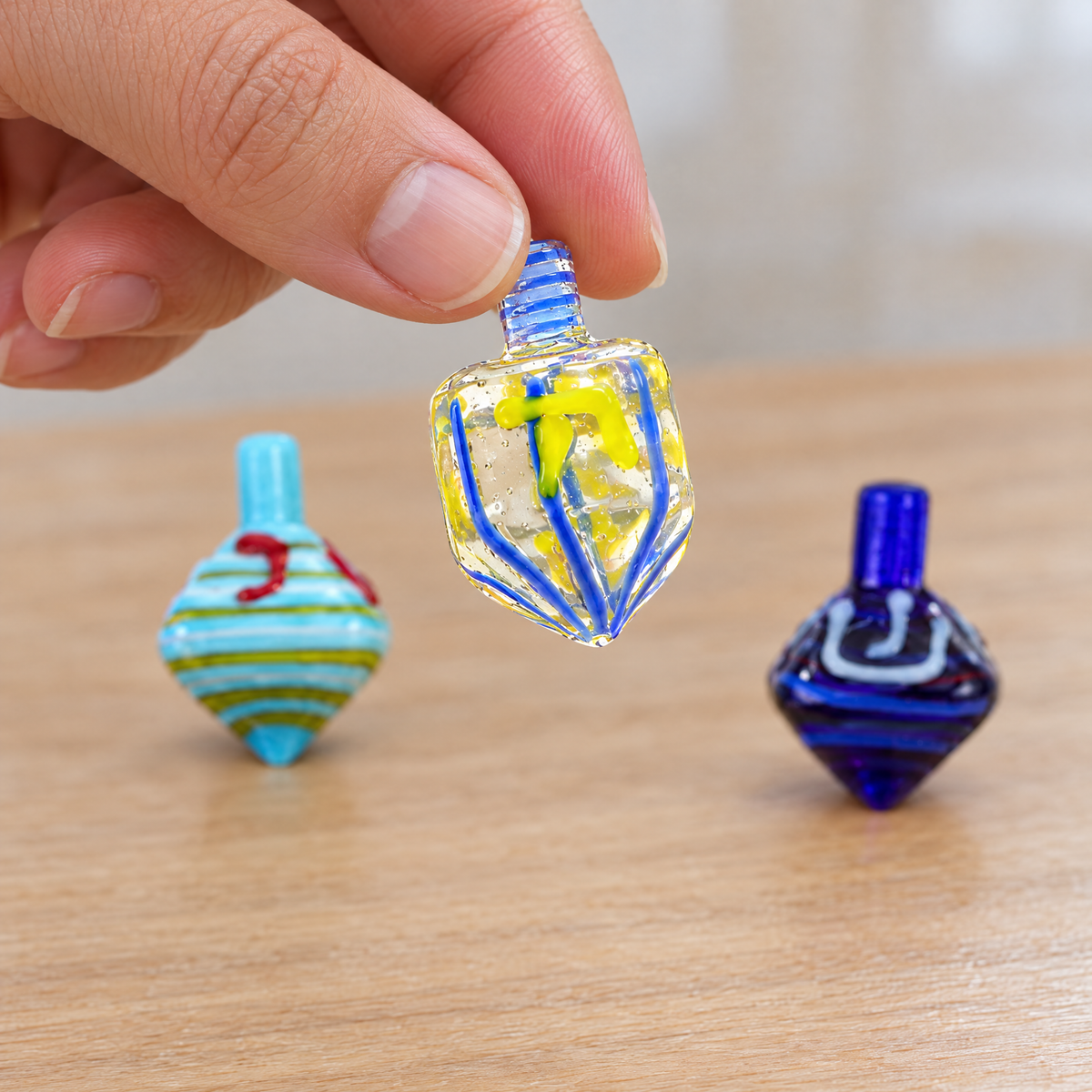 Glass dreidel held between two fingers, shown at real size